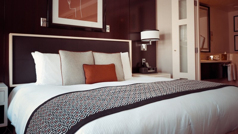 Hotel room Double bed with white bedding, gray and orange pillows, geometric patterned throw, and dark headboard in a hotel room.